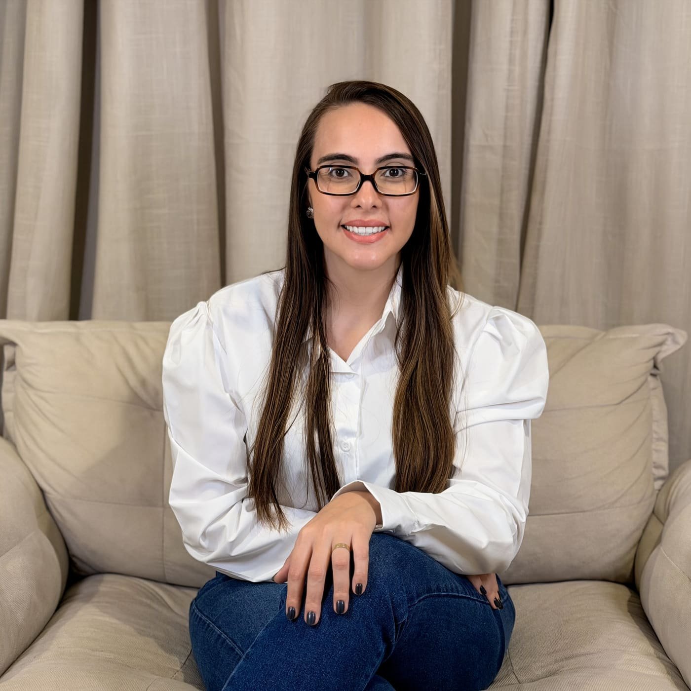 Laura Figueira, psicóloga, sorrindo sentada em um sofá bege
